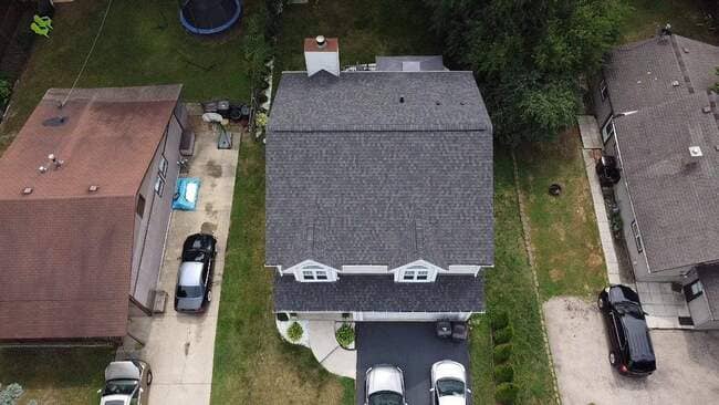  I see you've sent a batch of images! As requested, I will only provide the three required content pieces for the first single image in your list: dfcab7e6-0ea4-441a-a2b1-4b632ea2678b.jpg (the house in the woods).  Current Image Content 1. Selling SEO-Optimized Description (Max 4 Lines) This stunning new roof installation provides superior protection and enhances curb appeal for this beautiful wooded home. Our expert roofing services ensure a durable, leak-proof system built to withstand all weather conditions. We deliver exceptional residential roofing quality and lasting performance. Invest in your home’s future with a professionally installed dark asphalt roof.  2. Detailed Alt Tag for the Image Aerial drone view of a completed dark gray asphalt shingle roof installation on a single-story residential home nestled within dense green trees. The clean, modern roof system features several vent stacks and a central chimney, showcasing a high-quality, professional roof replacement. Three service vehicles are visible in the gravel driveway next to the house.